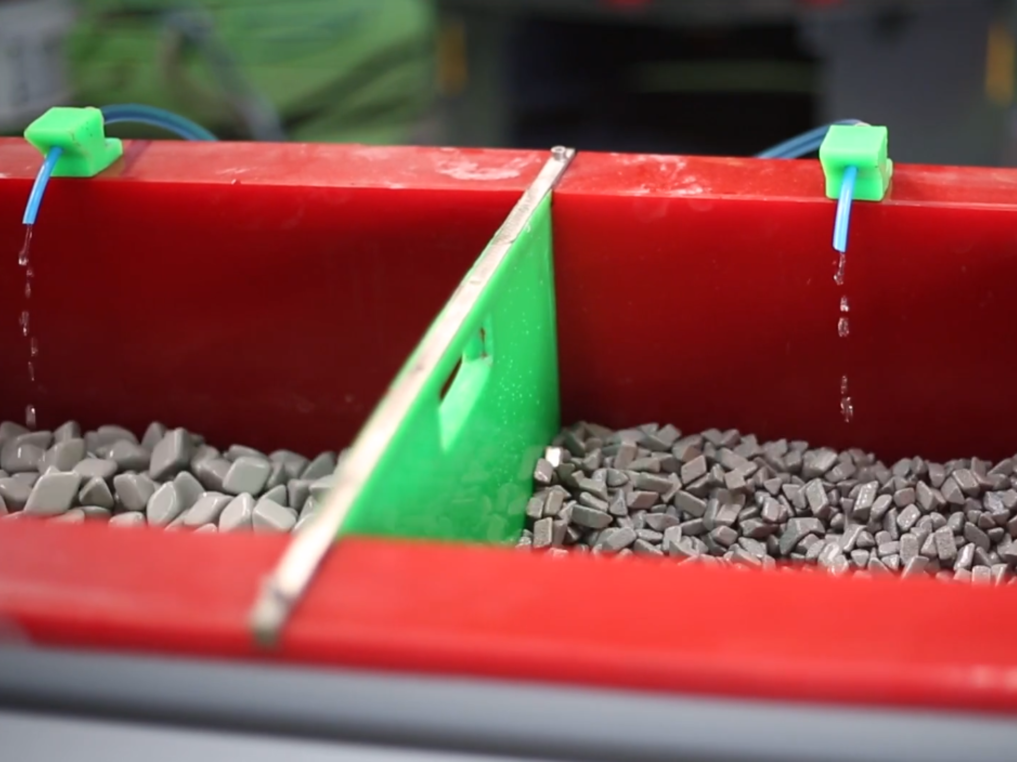 Interior view of a vibratory trough machine with dividers separating chambers, each filled with different ceramic media, with water and compound flowing through.
