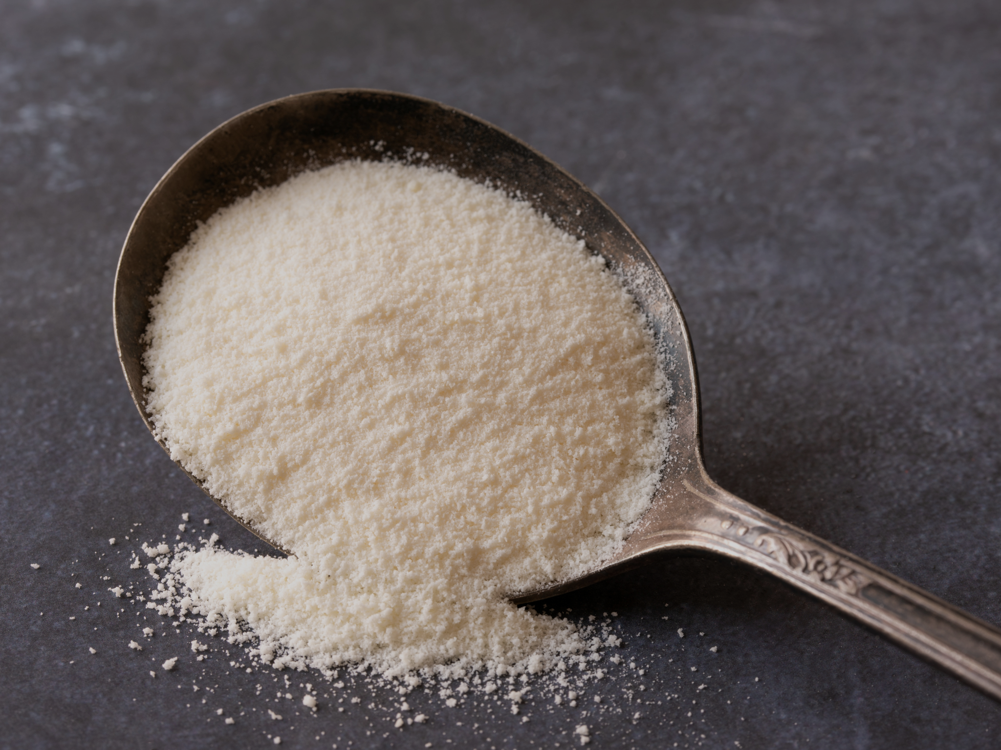 Spoon holding a fine portion of SX-81 powder compound, used in vibratory surface finishing for precision application and consistent results.