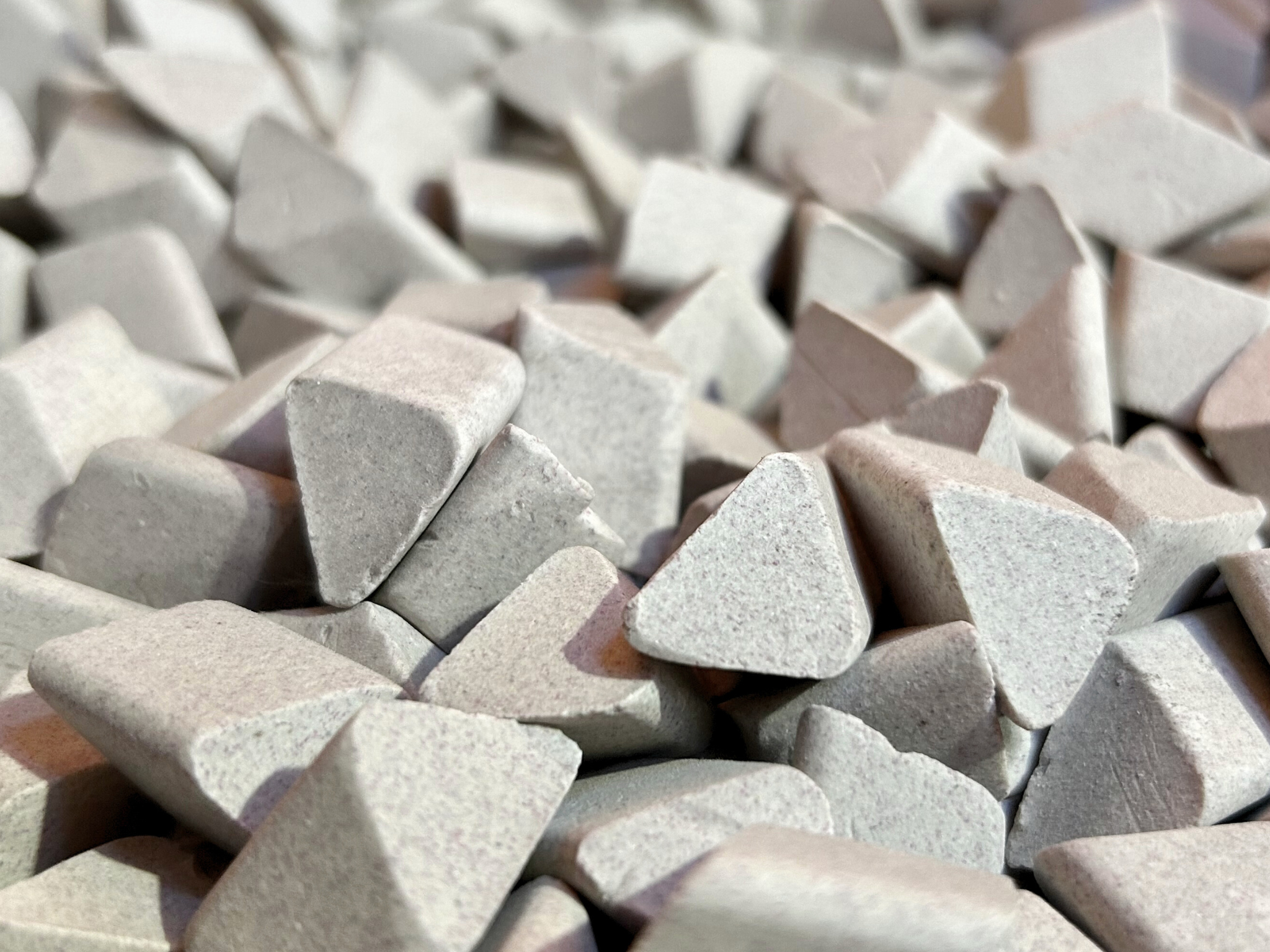 Close-up of triangular grey ceramic media, used in vibratory surface finishing for deburring and polishing metal parts.