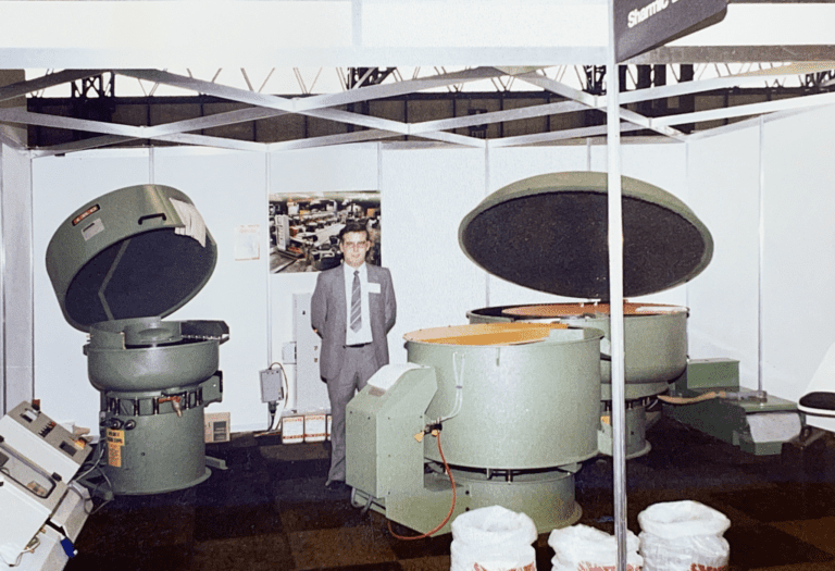 Brian, Founder of Sharmic Engineering, at Exhibition with Product Display Brian, founder of Sharmic Engineering, at an exhibition many years ago with media bags, machinery, and control panels displayed.