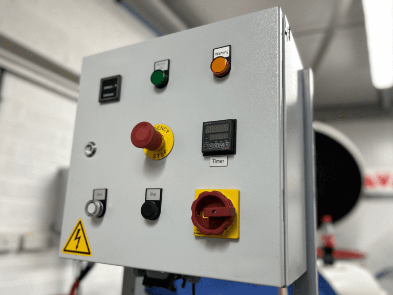Control panel for vibratory finishing machines displaying buttons for Stop, Start, Isolator, Emergency Stop, Timer, and Overall Hour Clock.