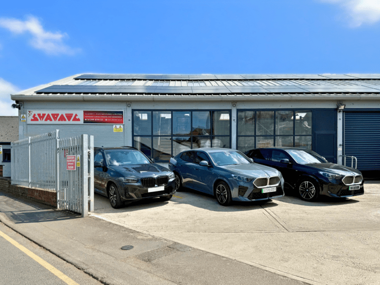 Front view of Sharmic Engineering headquarters featuring two electric vehicles, one hybrid vehicle in the parking area, and solar panels installed on the roof.