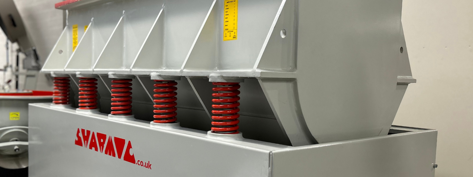 Side view of a vibratory trough finishing machine featuring the Sharmic logo and prominent suspension springs.